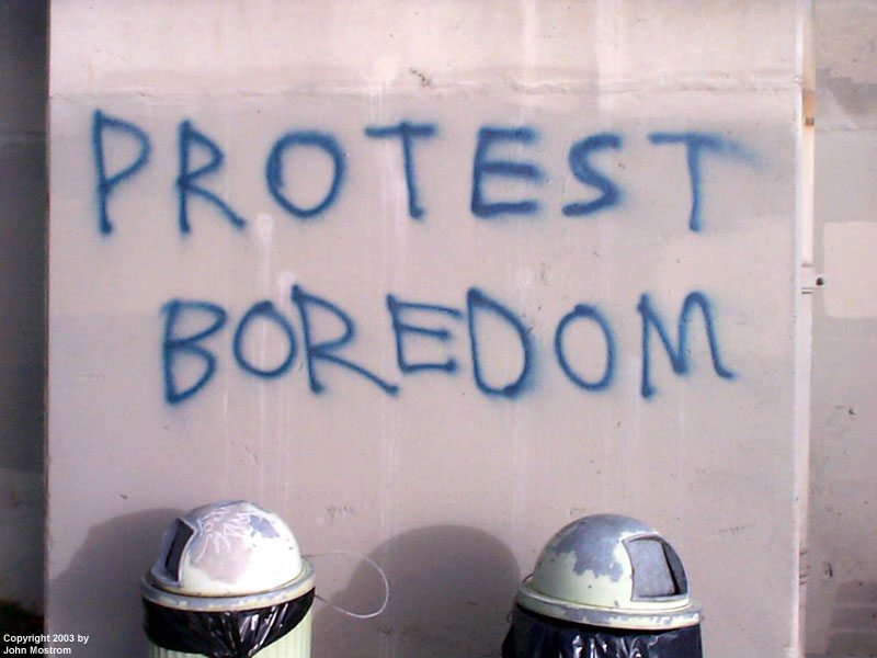Grafitti sprayed on a concrete wall: "PROTEST BOREDOM".